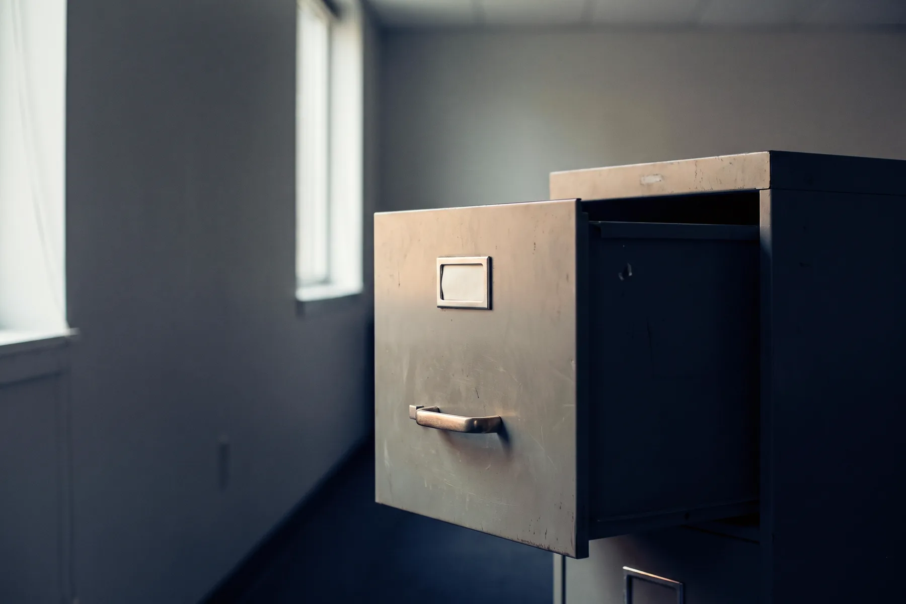 A single closed steel filing drawer in a quiet corridor, softly lit from one side.